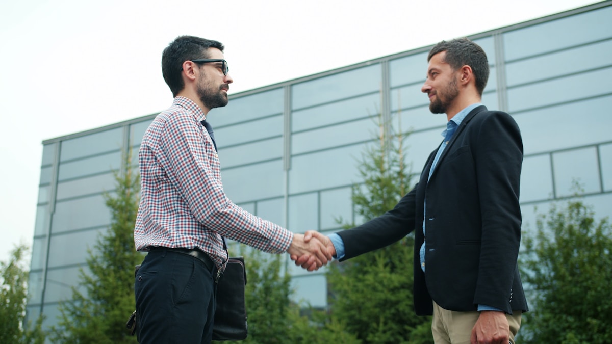 Two Magnus Kor talent partners shaking hands outside a modern office, representing the Associate Partner Programme